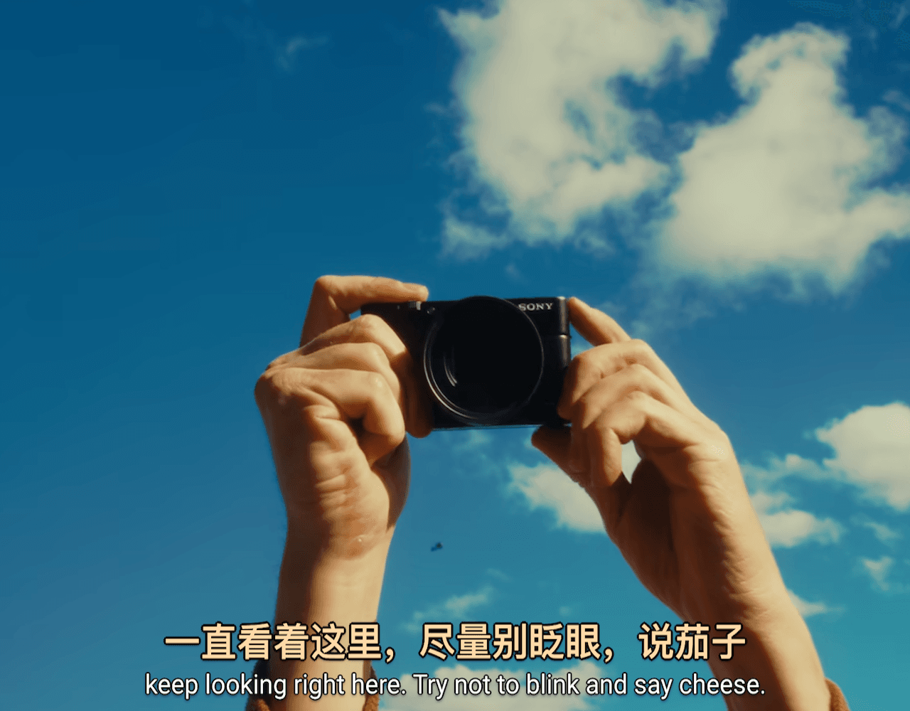 拍照场景的正确翻译：一直看着这里，尽量别眨眼，说茄子。英文字幕为 keep looking right here. Try not to blink and say cheese.